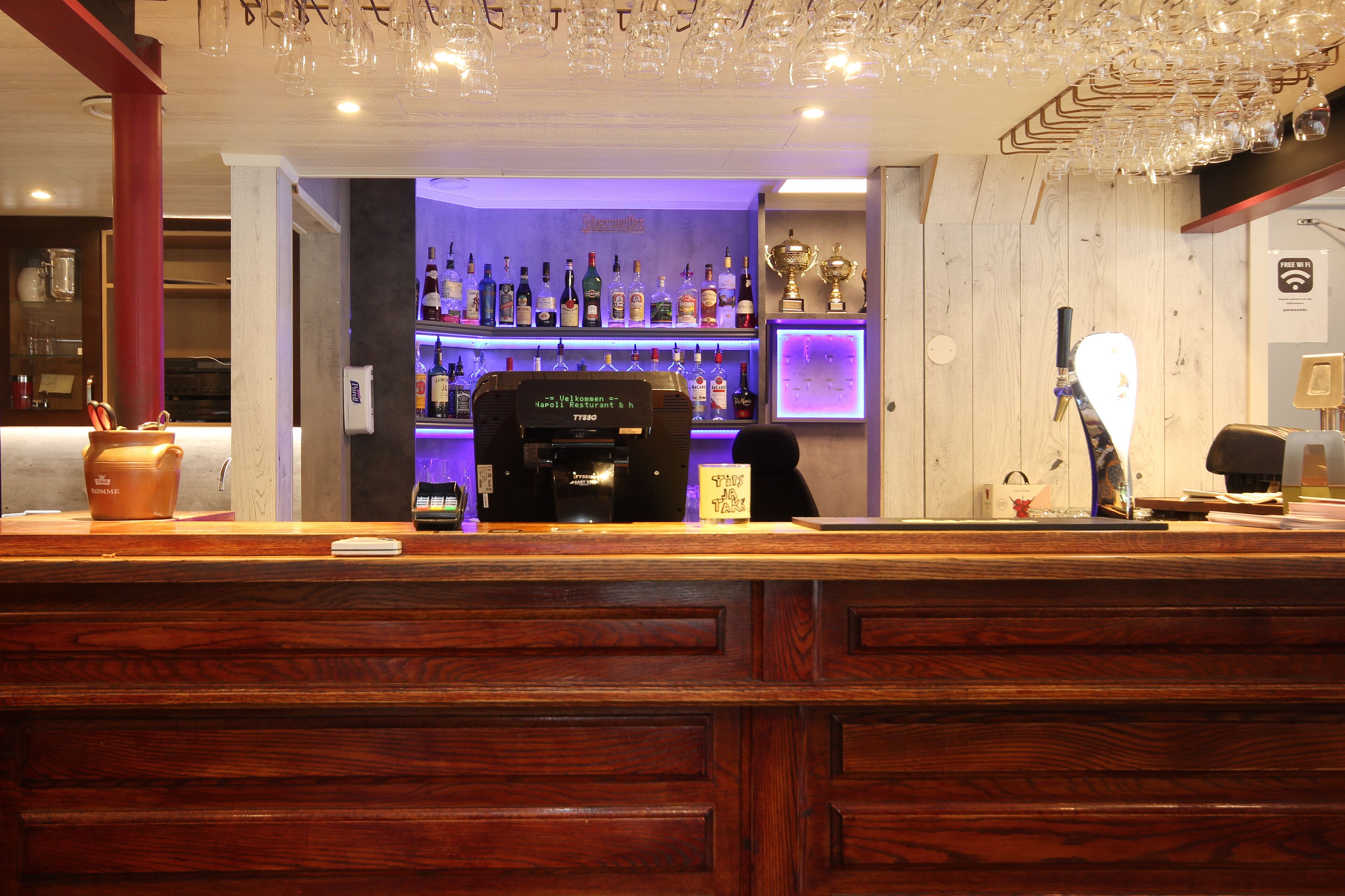 A bar area with a wooden counter, a coffee machine, and shelves stocked with bottles.