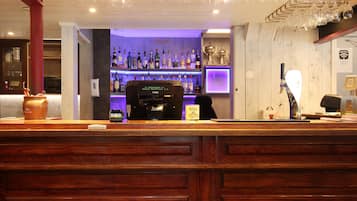 Una zona de bar con mostrador de madera, una máquina de café y estantes llenos de botellas.