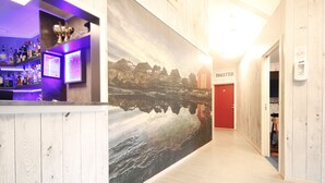 A bar area with a wooden counter and shelves of bottles, a large mural of a mountainous landscape, and a red door labeled "TOILETTER". - Napoli resturant & Hotell (Alstahaug)