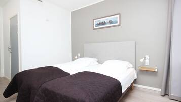 Een tweepersoonsbed met een grijs hoofdbord, een nachtkastje met een lamp en een ingelijste foto aan de muur.