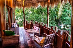 A wooden deck with a thatched roof, furnished with a table, chairs, and a swing.