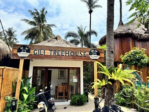 A treehouse named Gili Treehouse with a thatched roof, surrounded by lush greenery and palm trees. - Gili Treehouses (Gili Trawangan)