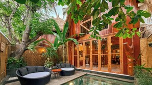 A pool area with a glass-enclosed structure, wicker furniture, and lush greenery. - Gili Treehouses (Gili Trawangan)