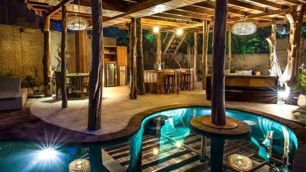 A pool area with a wooden deck, lounge chairs, and a bar area. - Gili Treehouses (Gili Trawangan)