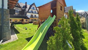 A wooden play structure with a green slide in a backyard. - Willa Wrzos (Zakopane)