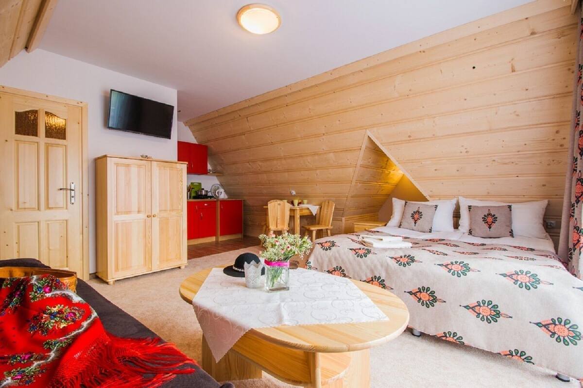 Un dormitorio acogedor con una cama, un armario de madera, una mesita con un jarrón y un televisor en la pared.