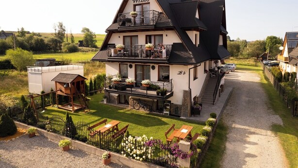 A two-story building with a balcony, a wooden deck, and a gravel driveway. - Willa Wrzos (Zakopane)