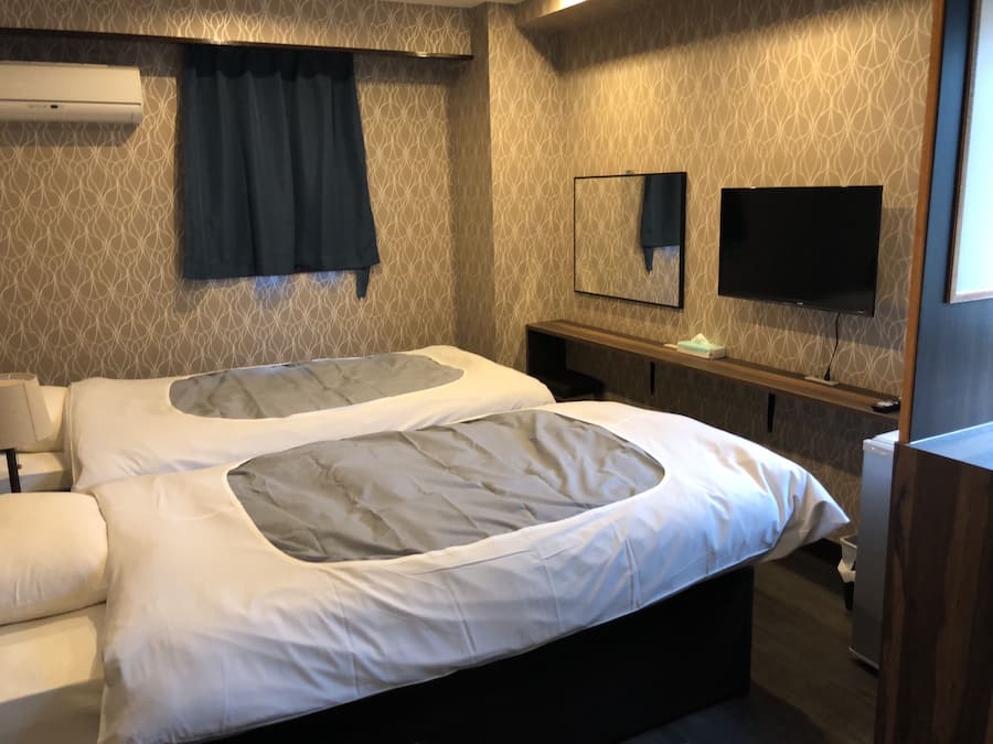 Een hotelkamer met een bed, nachtkastje, lamp, televisie en spiegel.
