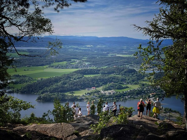 A panoramic view of a lake surrounded by forested hills and a small town. - Kleivstua (Hole)