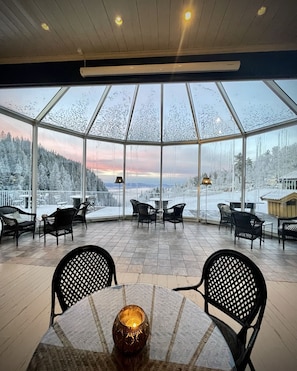 Ein gläserner Raum mit Blick auf eine verschneite Landschaft und einen Sonnenuntergang.