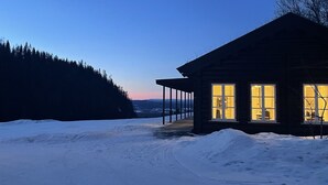 Una cabaña de madera con un porche, rodeada de nieve y un paisaje boscoso.