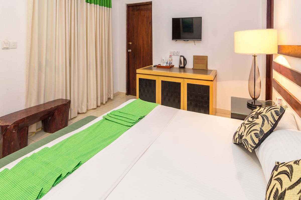 A hotel room with a bed, a wooden bench, a TV, a cabinet, and a lamp.