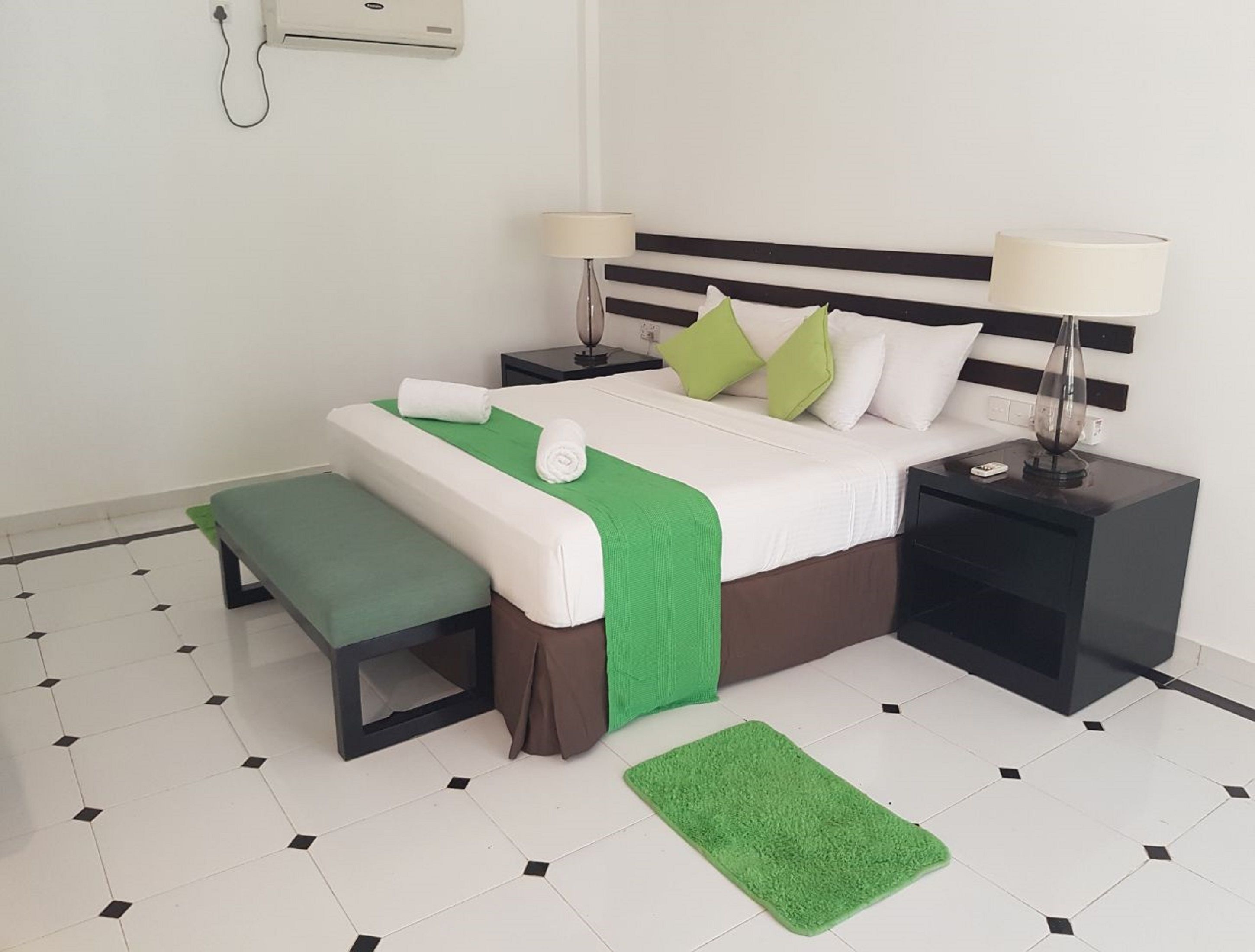 A neatly arranged hotel room with a bed, bedside tables, a bench, and a green rug.