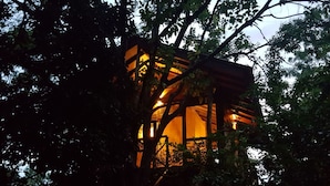 A treehouse with a wooden exterior and a warm interior light. - Eighth Wonder Resort (Sigiriya)
