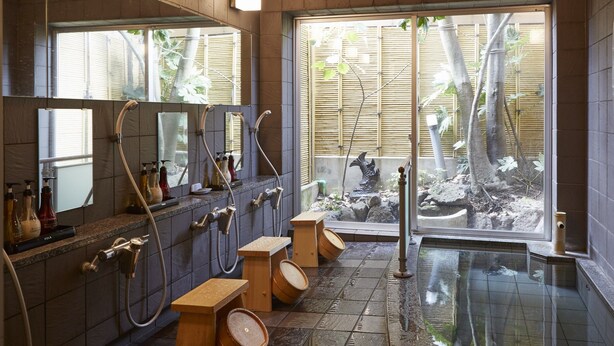 Un bagno moderno con diverse doccette, sgabelli di legno e un'ampia finestra vista bambù e rocce.