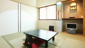 Una tradizionale stanza giapponese con pavimento in tatami, un tavolino, una televisione e un'anta scorrevole.