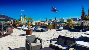 A beachside lounge area with lounge chairs and umbrellas, overlooking a cityscape with notable buildings and a flag. - Sky Business Hotel (Legnica)