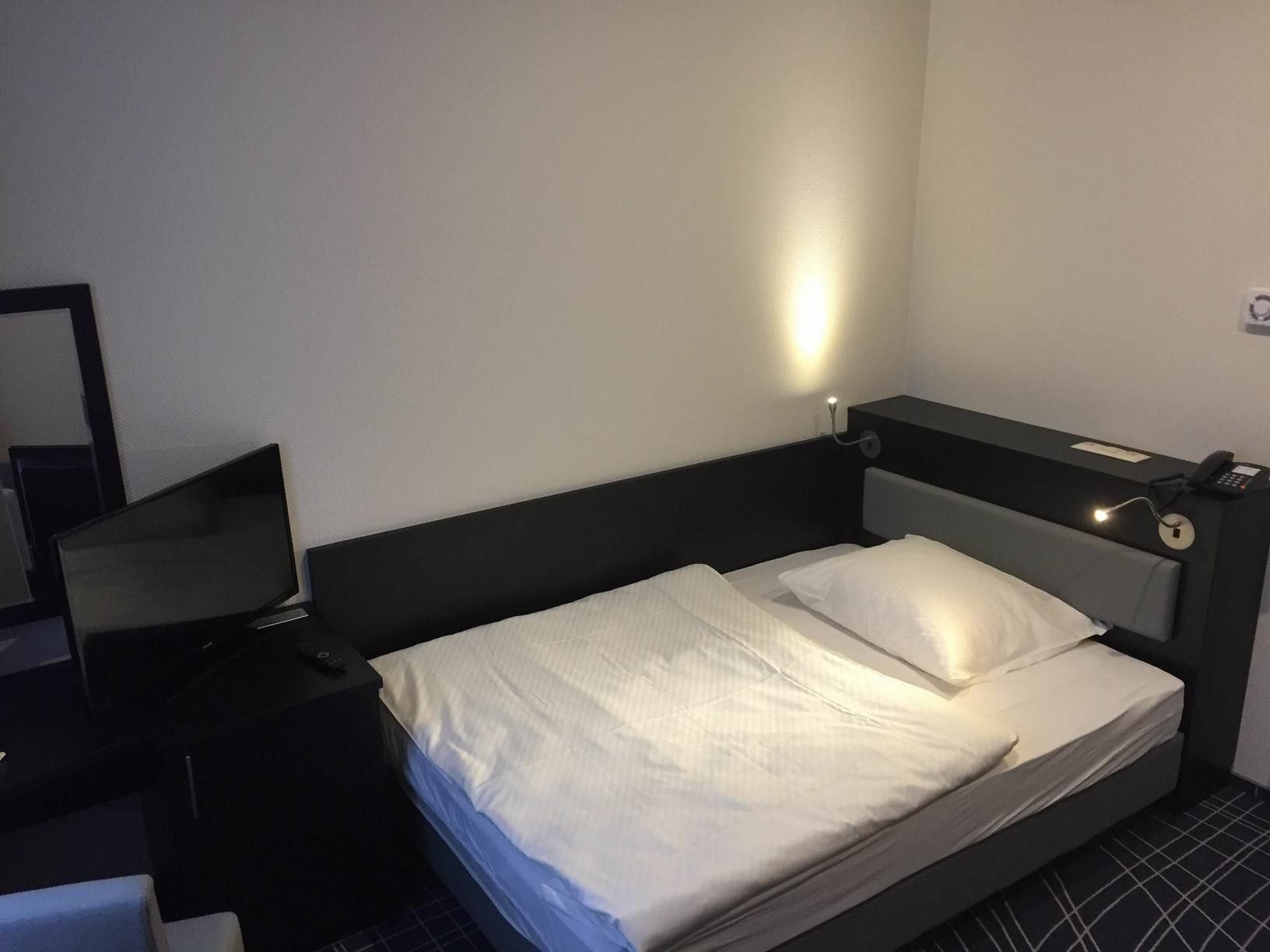 Una habitación de hotel con una cama individual, una mesita de noche, una lámpara y un espejo.