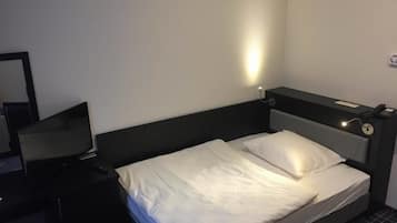 Una habitación de hotel con una cama individual, una mesita de noche, una lámpara y un espejo.