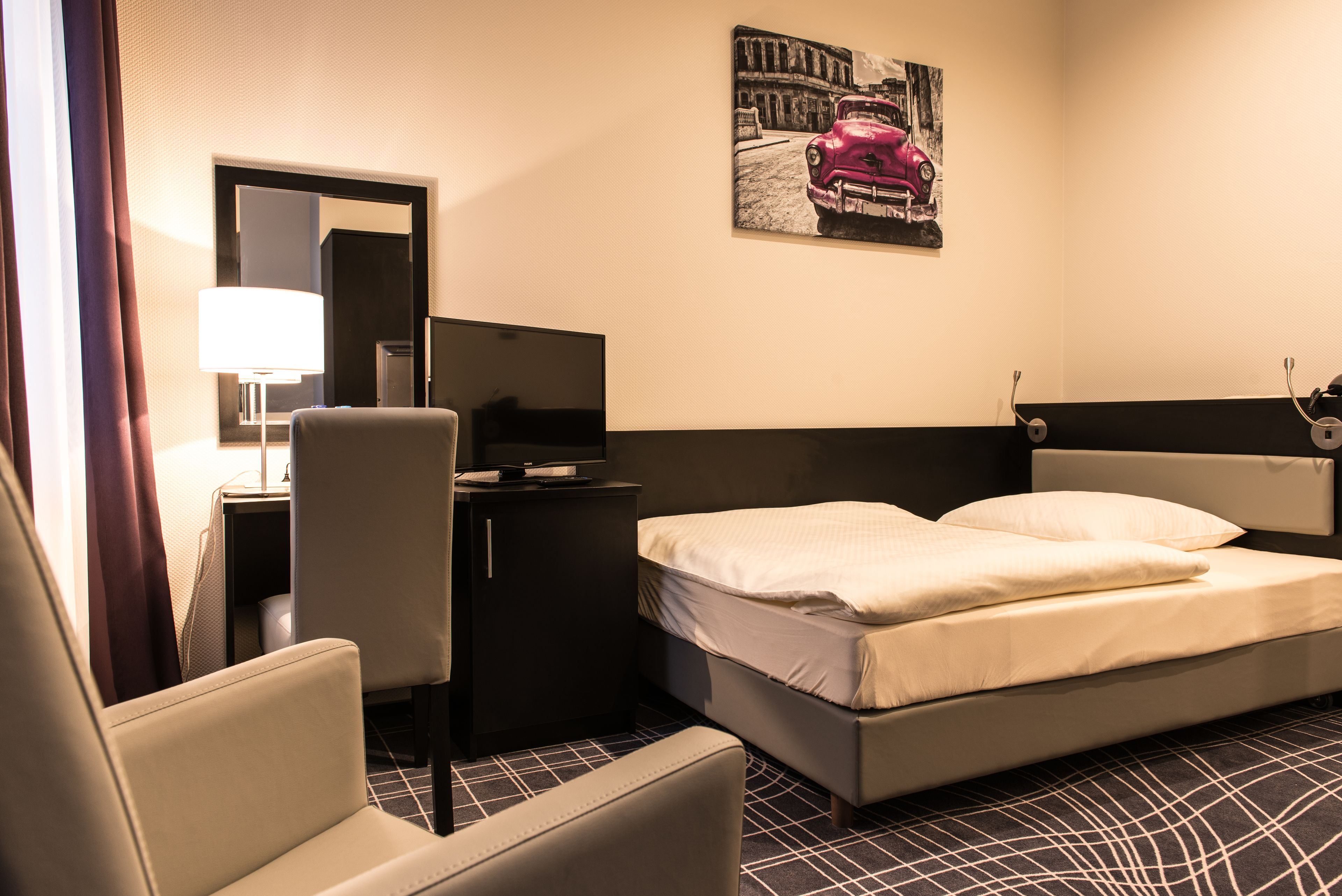 Une chambre d’hôtel avec un lit, un bureau avec une lampe, une chaise et un téléviseur.