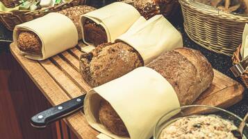 A wooden cutting board with several loaves of bread wrapped in paper, a knife, and a bowl of spread.