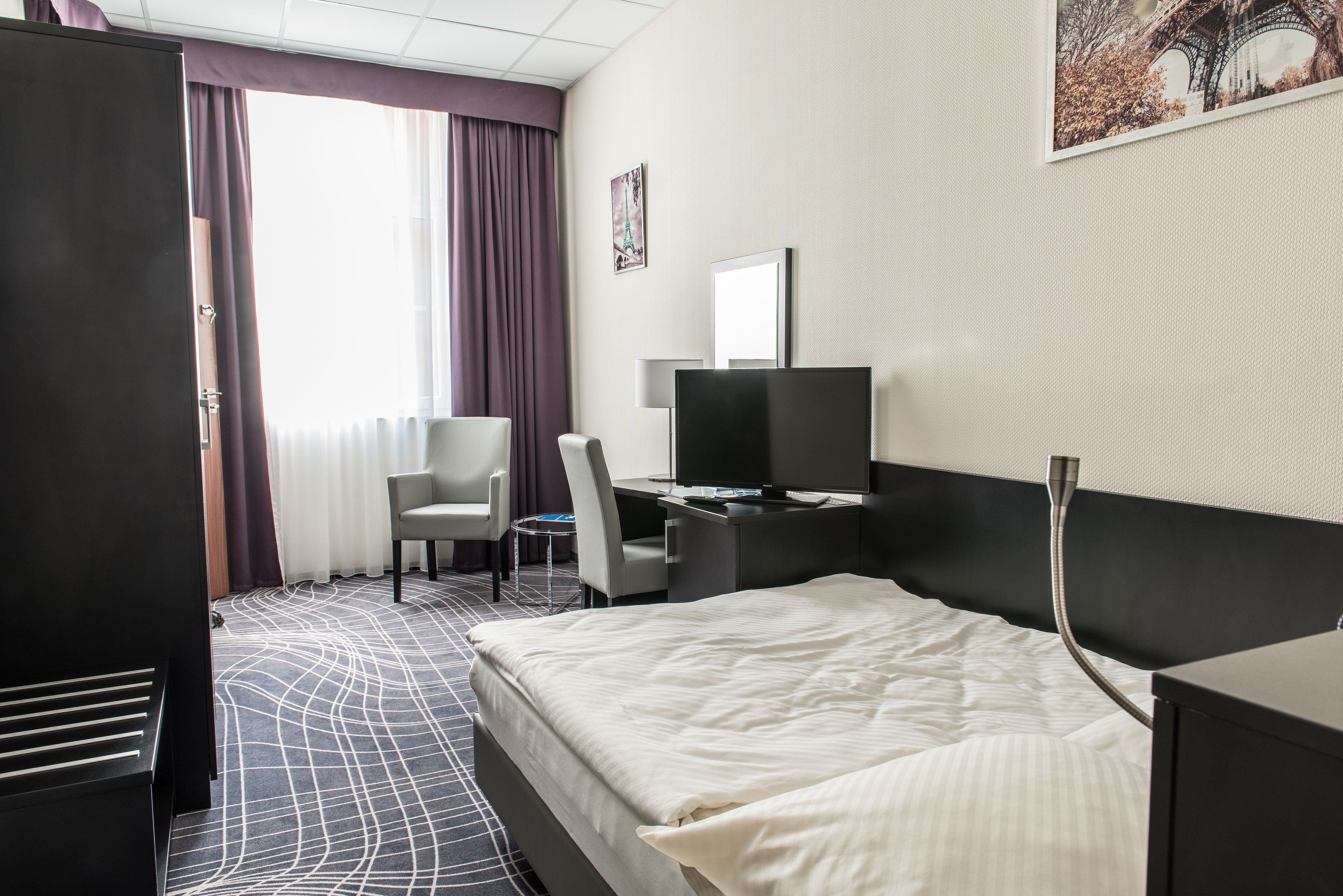 Une chambre d’hôtel comprenant un lit, un bureau, une chaise, un téléviseur et une armoire.