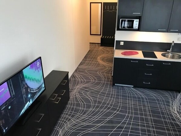 A modern kitchen with a black countertop, a microwave, and a flat-screen TV on a stand.
