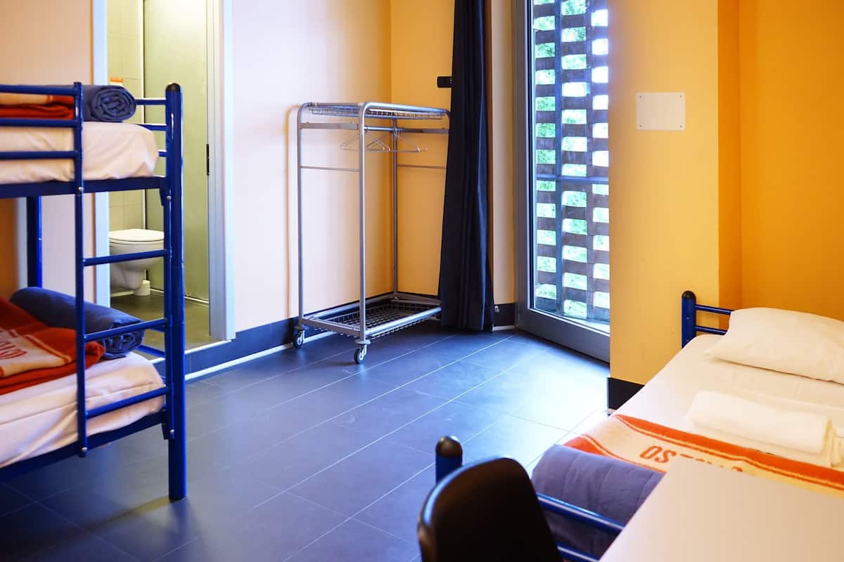 Une pièce avec des lits superposés, un étendoir métallique, une fenêtre donnant sur un paysage agréable et des toilettes.