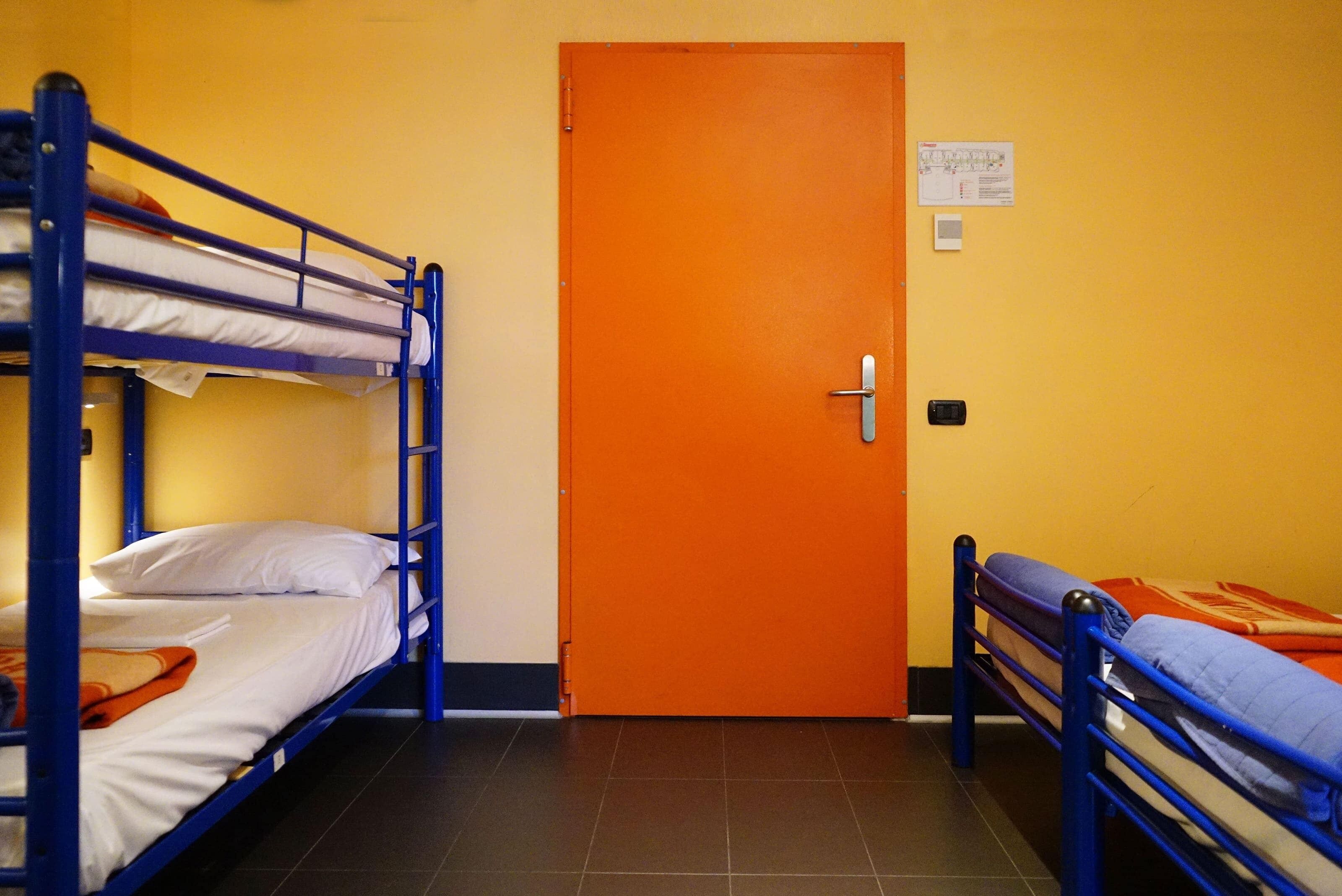 A dormitory room with bunk beds, an orange door, and a small notice on the wall.