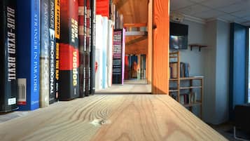 A wooden bookshelf with books in a room with a tiled ceiling and a television on the wall.
