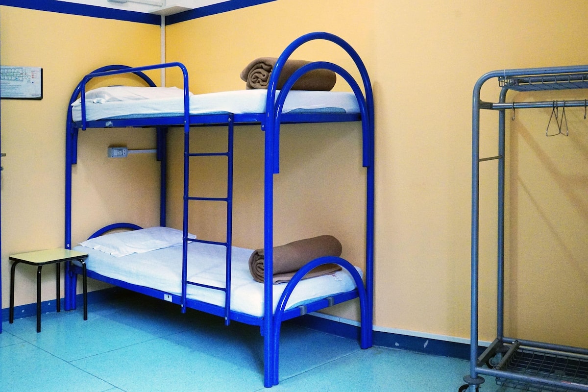 Une chambre avec un lit superposé, une petite table et un étagère en métal.
