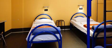 A dormitory room with bunk beds and a small stool.