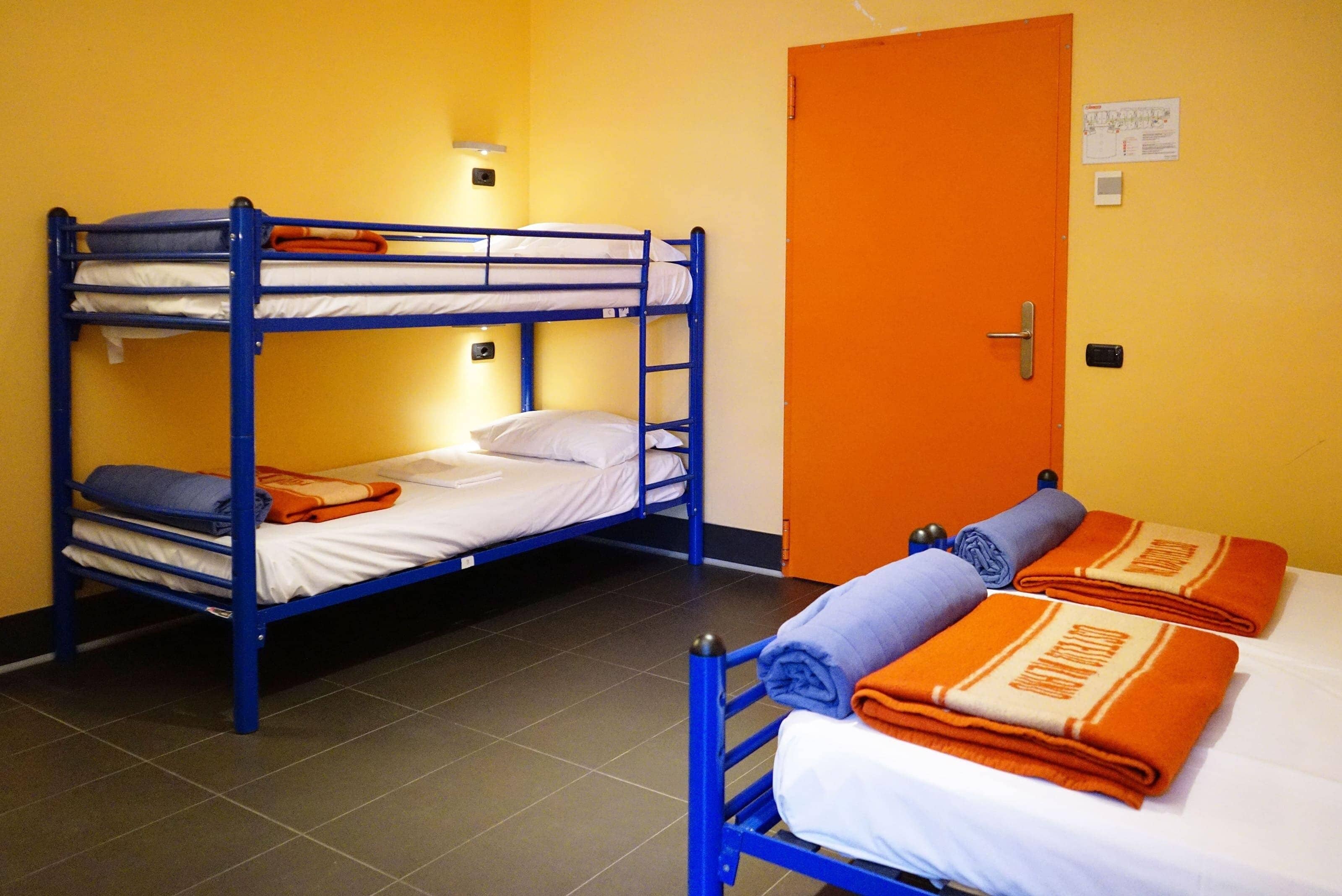 Une chambre de dortoir avec des lits superposés, une porte et un luminaire fixé au mur.