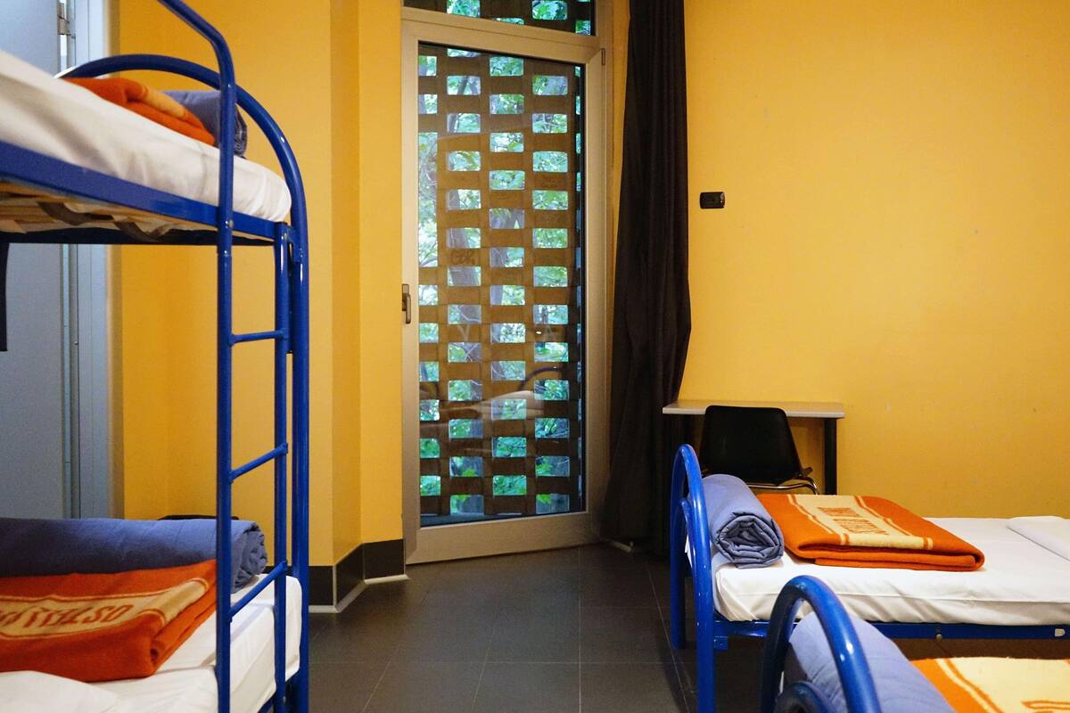 Une chambre de dortoir avec des lits superposés, un bureau et une fenêtre donnant sur un paysage verdoyant.