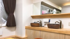 A bathroom with a wooden vanity, two brown ceramic bowls, a brass faucet, a mirror, and a trash can. - Hostel Mallika (Hiroshima)