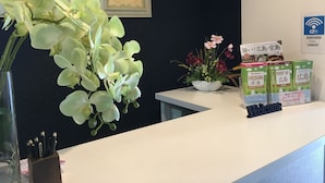 A reception desk with a vase of orchids, a framed floral artwork, and informational brochures. - Hostel Mallika (Hiroshima)