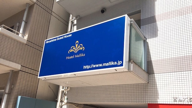 A blue sign for Hostel Mallika, indicating a guest house with a website URL. - Hostel Mallika (Hiroshima)