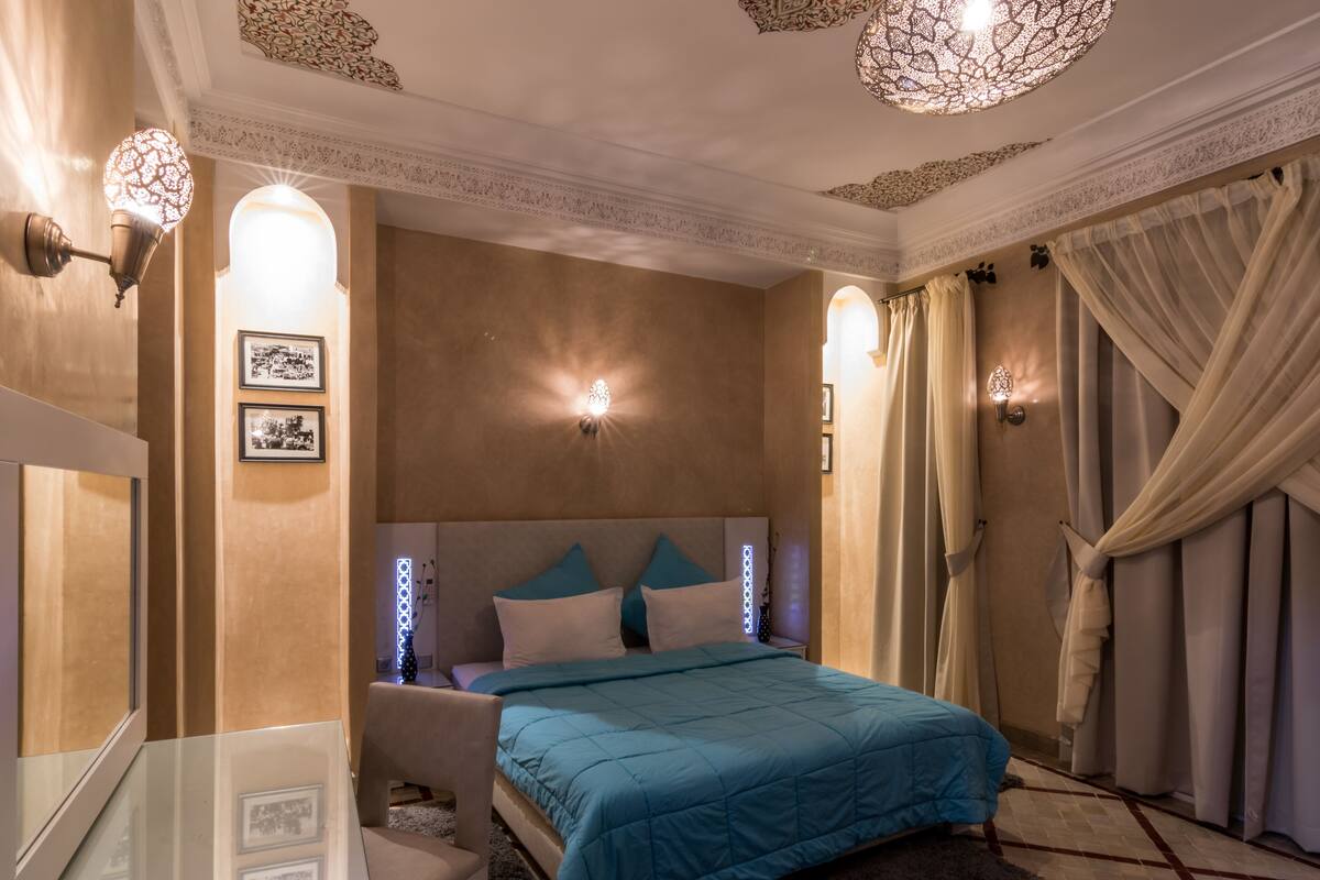 Quarto com cama, mesas de cabeceira e arandelas.