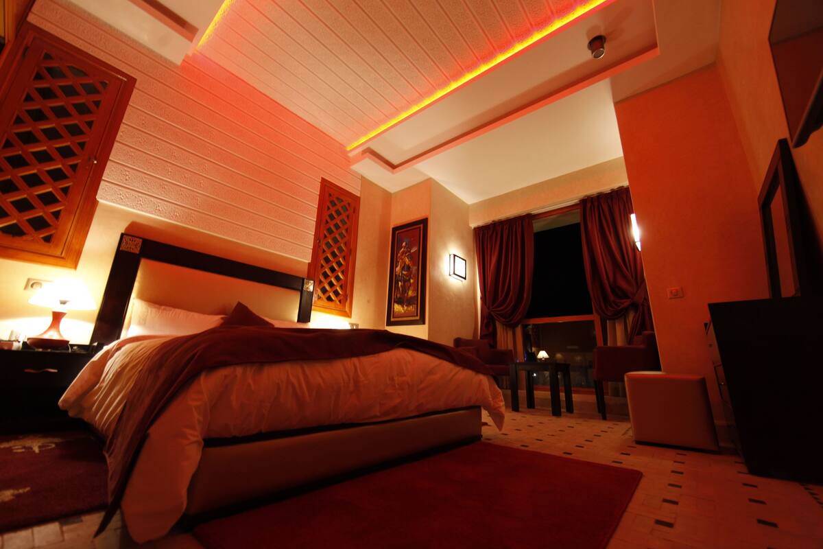 Quarto de hotel com cama, escrivaninha, cadeira e televisão.