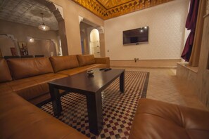 Un salon avec un canapé en cuir marron, une table basse en bois et un tapis à motifs.