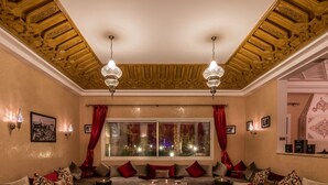 Un salón acogedor con un conjunto de sofás, una mesa de centro y dos mesitas auxiliares. Hay un ventanal con cortinas, una araña y luces empotradas en la pared.
