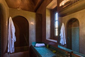 Une salle de bain avec une baignoire, une douche et un lavabo. Des serviettes sont accrochées au mur et une fenêtre laisse entrer la lumière naturelle.
