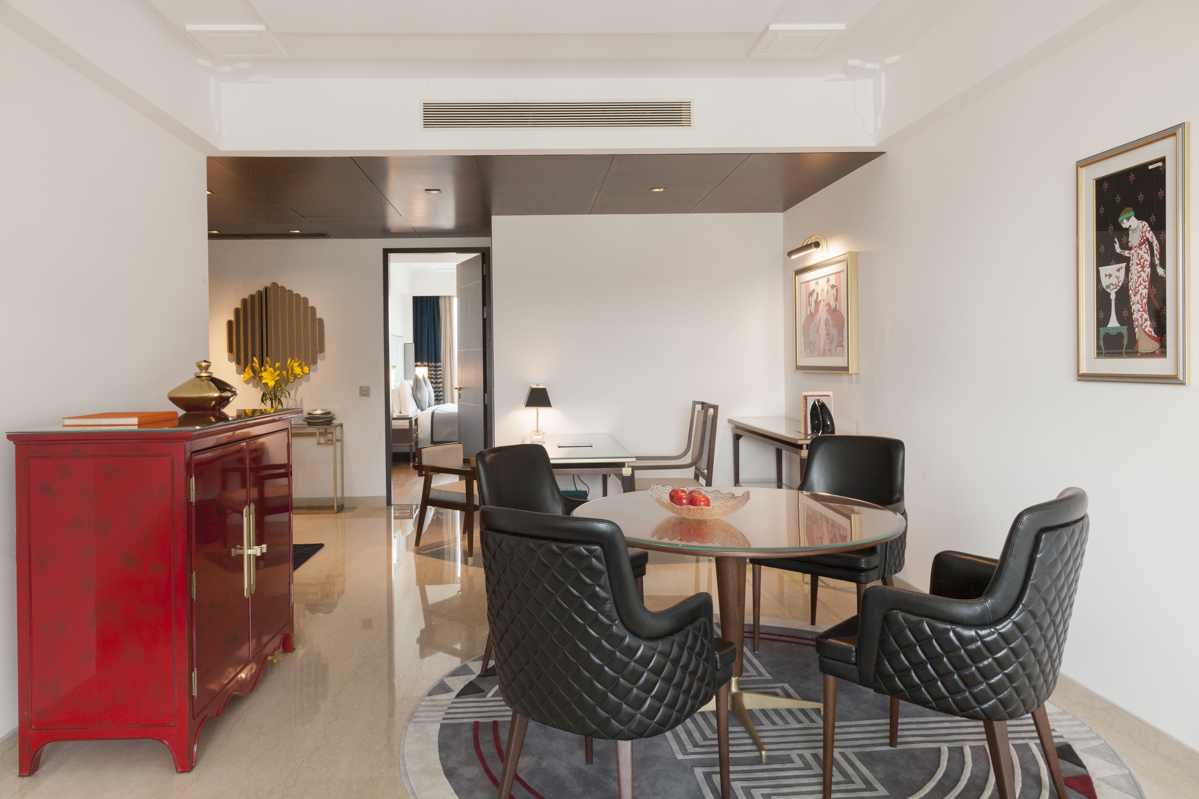 A modern dining area with a round glass table, black upholstered chairs, and a red cabinet.