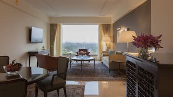 A hotel room with a dining area, a sofa, a TV, and a view of the outdoors.