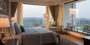 A hotel room with a large bed, a chair, a table, and a view of the city.