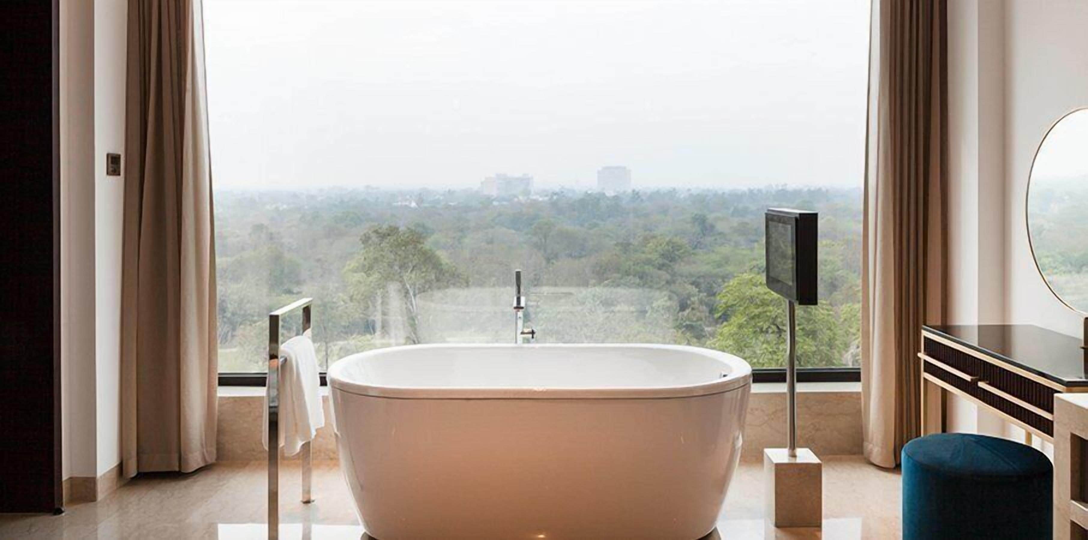 A modern bathroom with a freestanding bathtub, a vanity with a mirror, and a view of a cityscape through large windows.