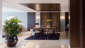 Un hall d’hôtel moderne comprenant un espace repas, une grande plante en pot et un mur décoratif orné de motifs géométriques.