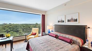A hotel room with a large bed, a desk with a laptop, a chair, and a view of a green landscape.