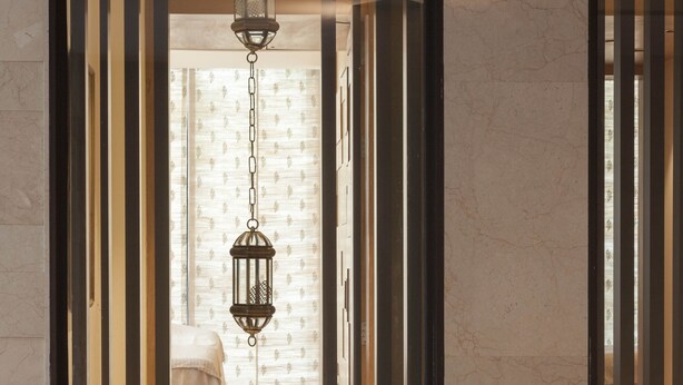 Un intérieur moderne avec une lanterne suspendue, un lit et une salle de bain visible à travers une cloison en verre.