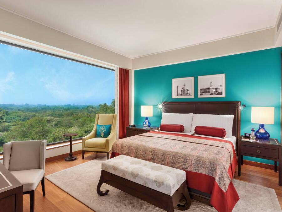 A hotel room with a large bed, two bedside tables, a desk, a chair, and a view of the outdoors.